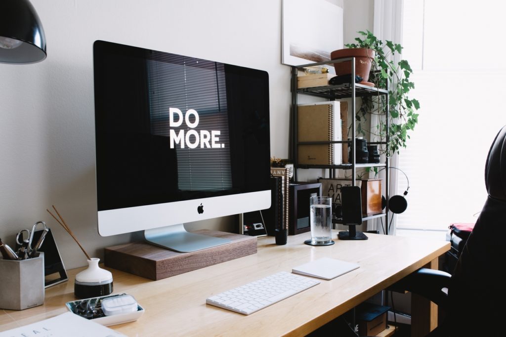 Office with close-up of a desk and Apple computer, chair and a rack with plant and books etc.