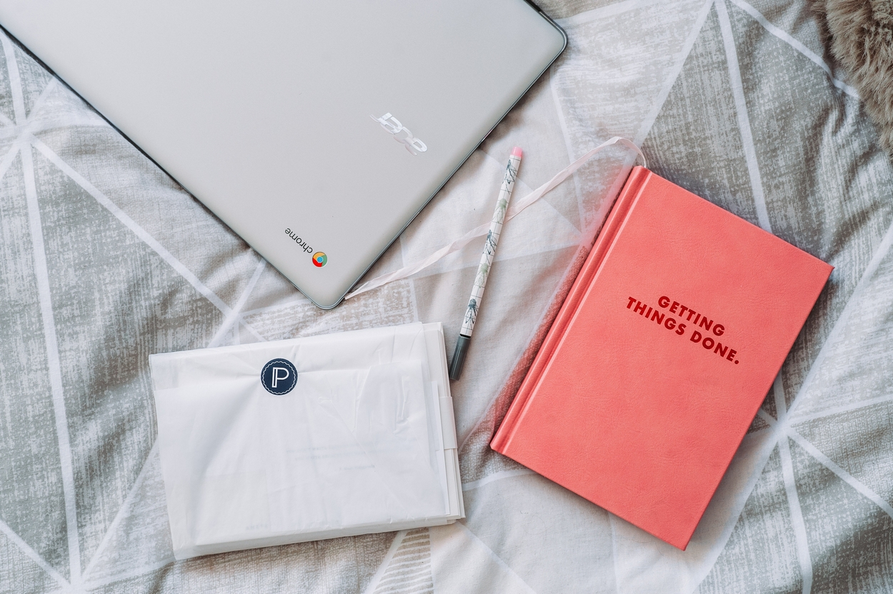 bed cover with closed laptop, and book with title getting things done