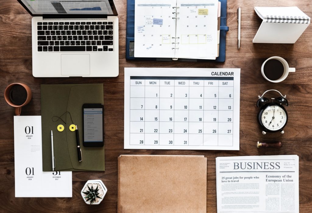 Desk with objects, laptop, calendar, agenda,2 coffeecups, newspaper, alarmclock